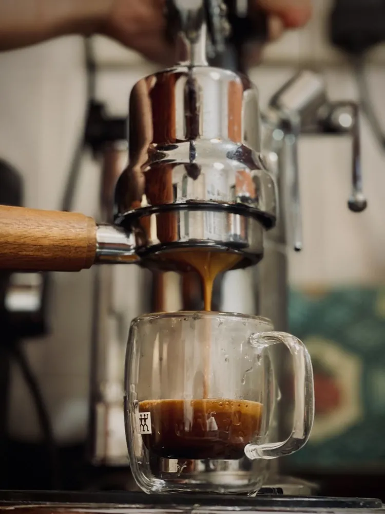 Espresso pouring from a lever machine into a glass cup
